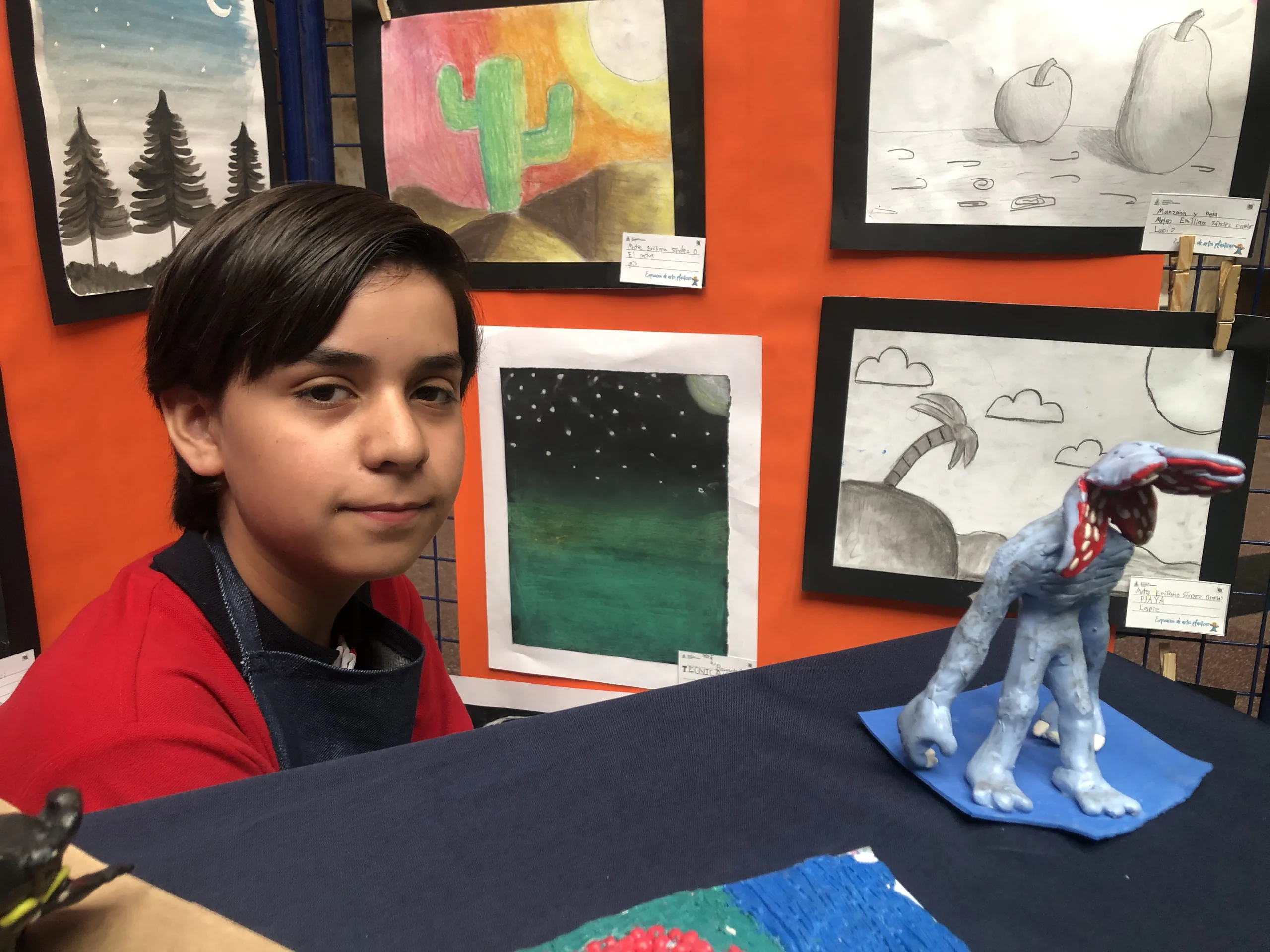 Alumno junto a sus dibujos y una escultura modelada