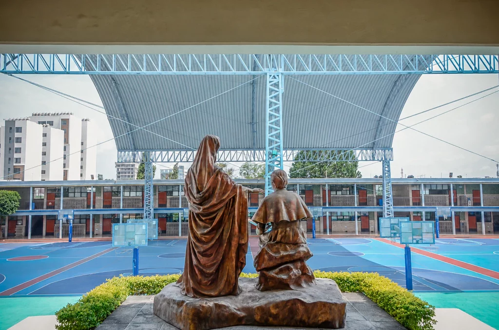 Escultura de bronce de Champagnat con niños frente a las canchas techadas