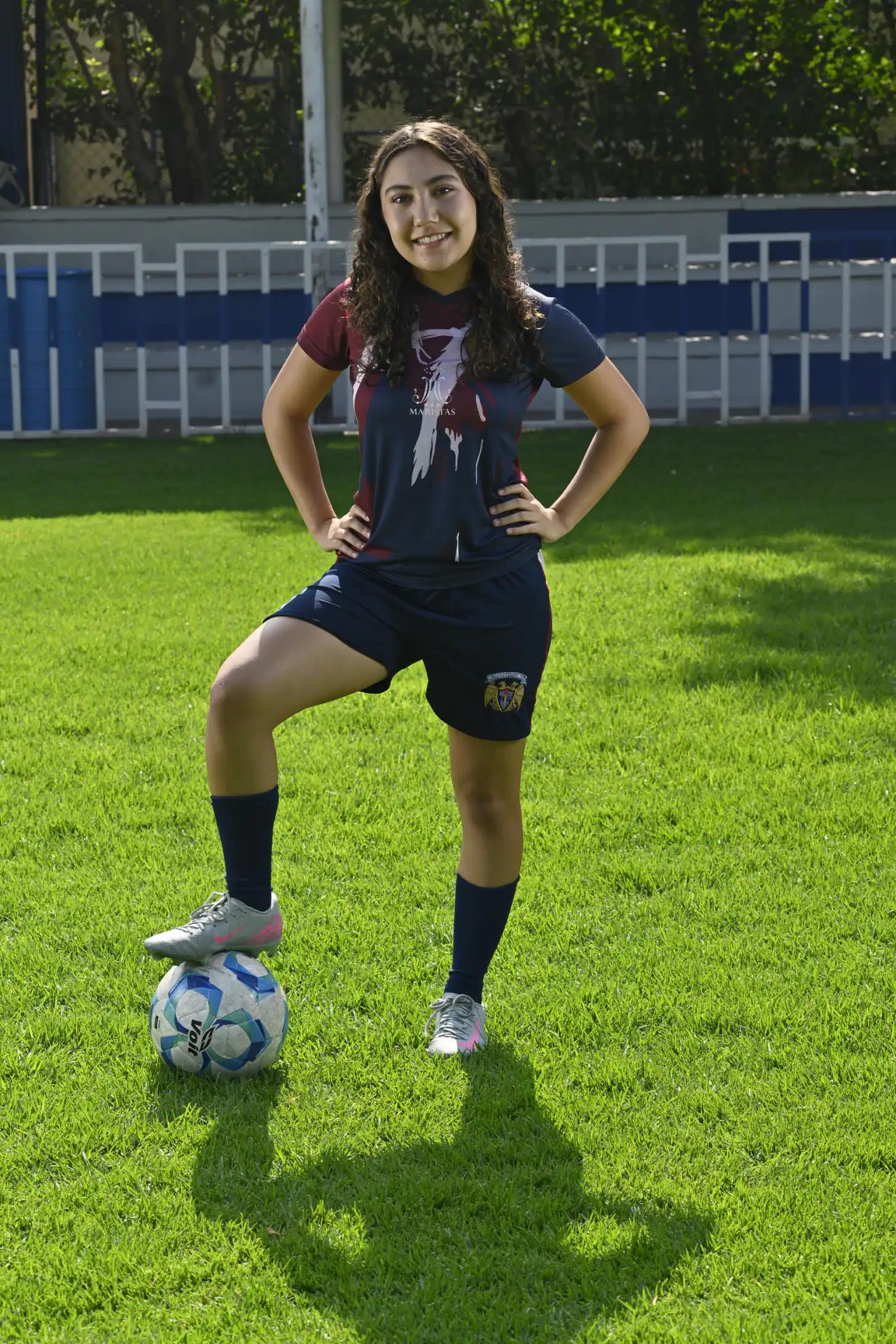 Alumna con uniforme de fútbol y balón frente a la tribuna