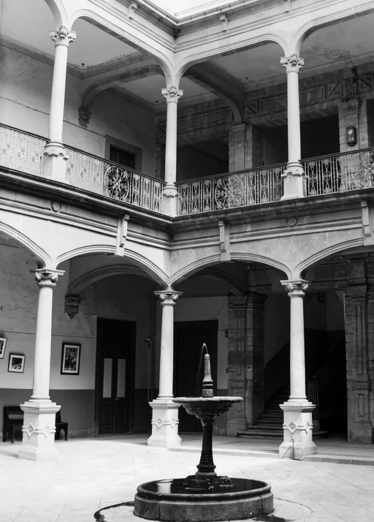 Patio colonial con fuente y arcos del edificio histórico, en blanco y negro