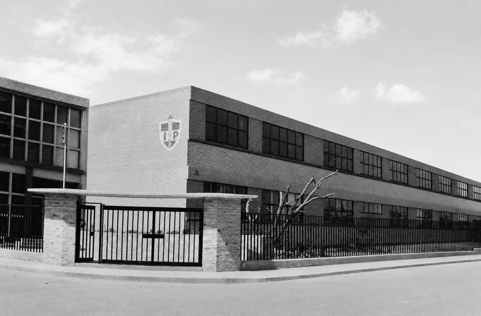 Edificio del nuevo plantel de Secundaria y Preparatoria con su reja y el escudo, en blanco y negro