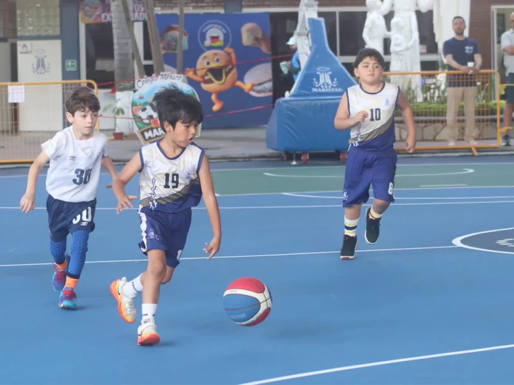Niños de primaria jugando básquetbol en la cancha azul