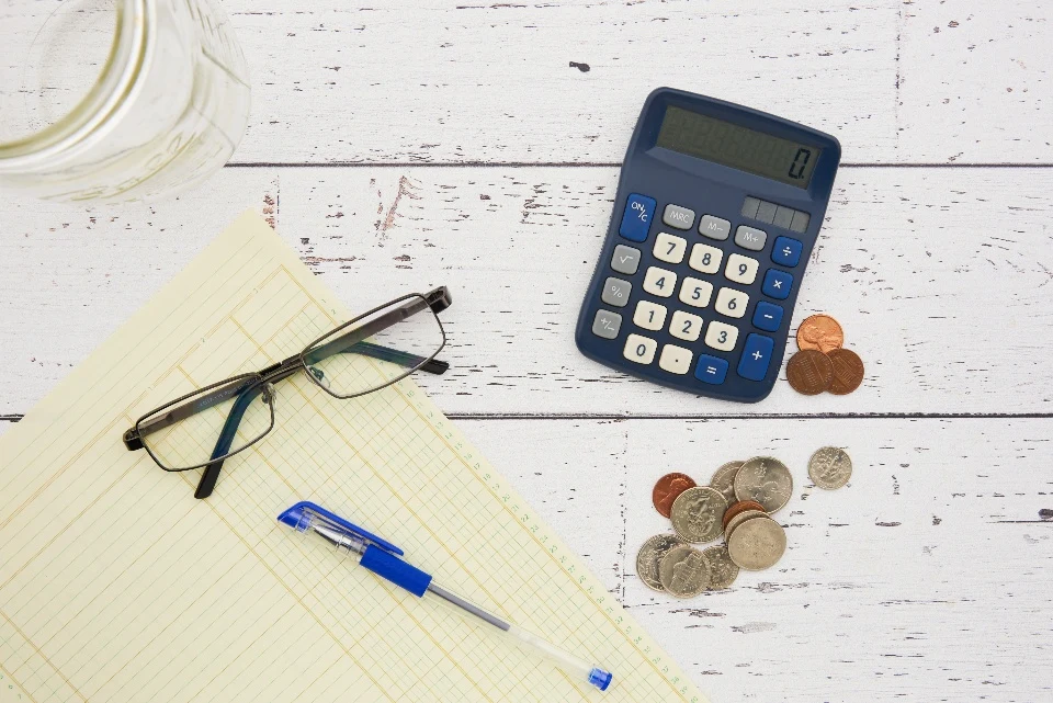 Lentes, pluma, calculadora y monedas sobre una mesa