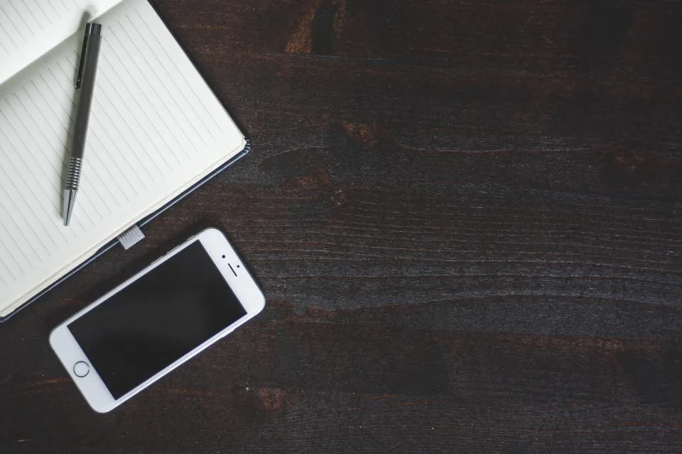 Teléfono celular, libreta y pluma sobre una mesa de madera oscura