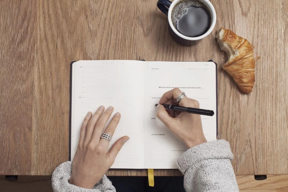 Manos escribiendo en una libreta junto a una taza de café