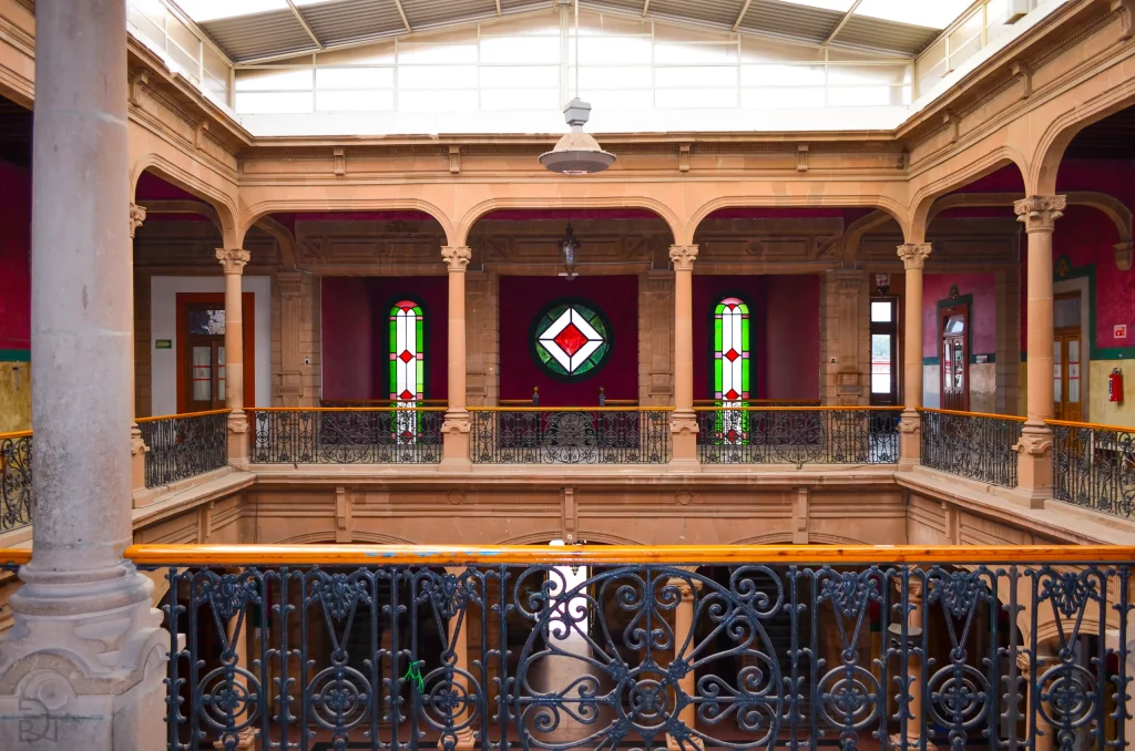 Patio interior de dos niveles bajo el lucernario, con balcones de hierro