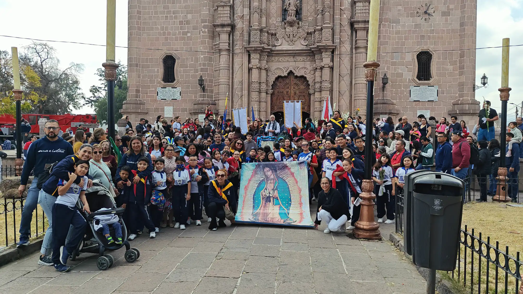 Comunidad escolar frente a un templo con el estandarte de la Virgen de Guadalupe