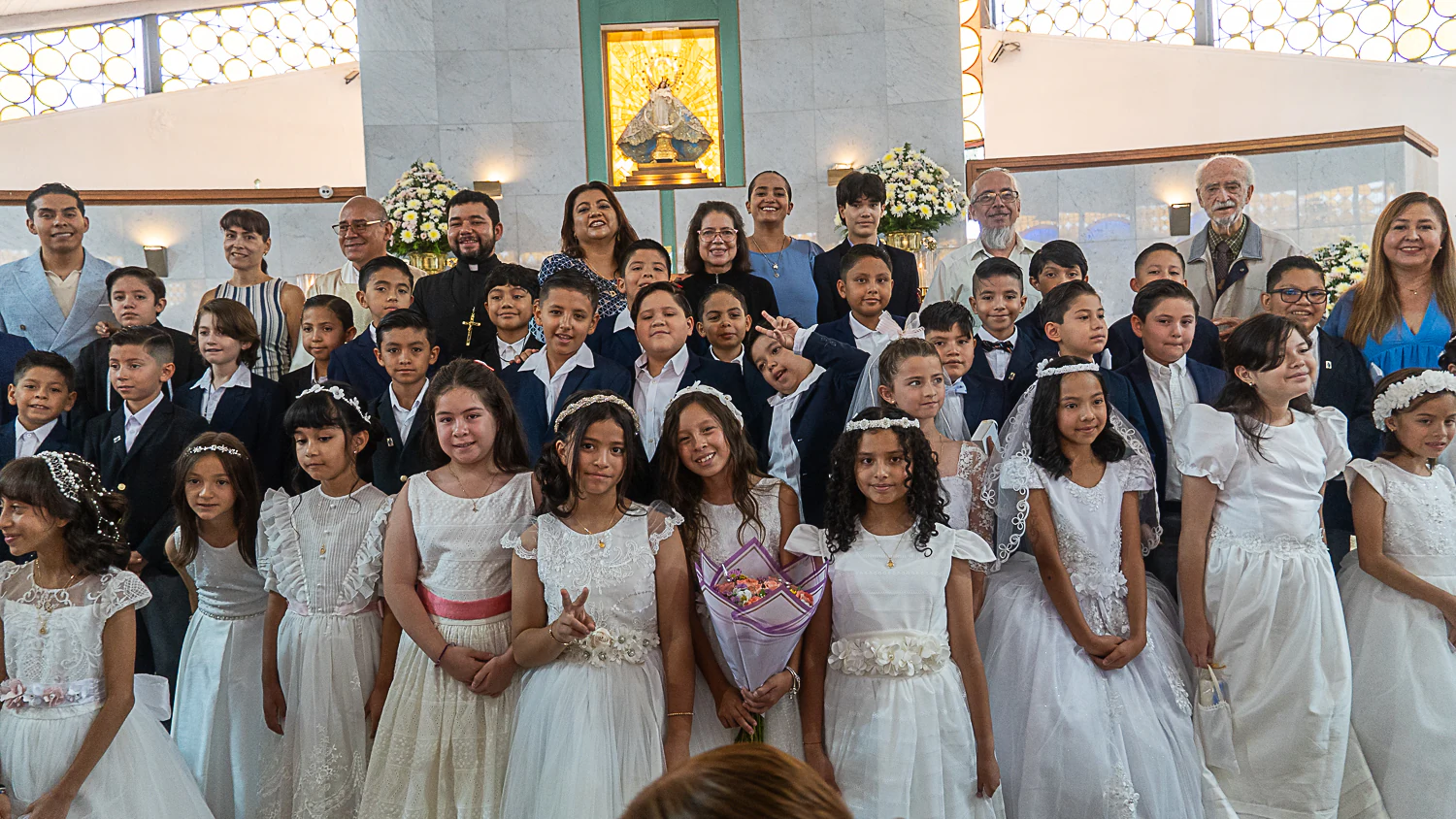 Niñas y niños de primera comunión, vestidos de blanco, con sus catequistas