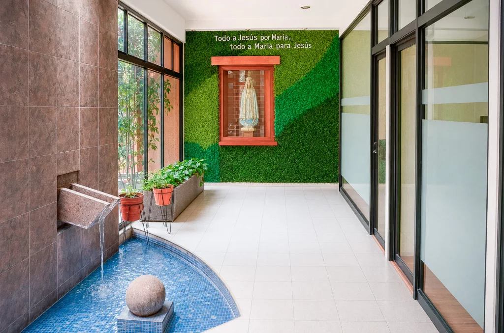 Muro verde con imagen de María y la frase «Todo a Jesús por María», junto a la fuente de la recepción