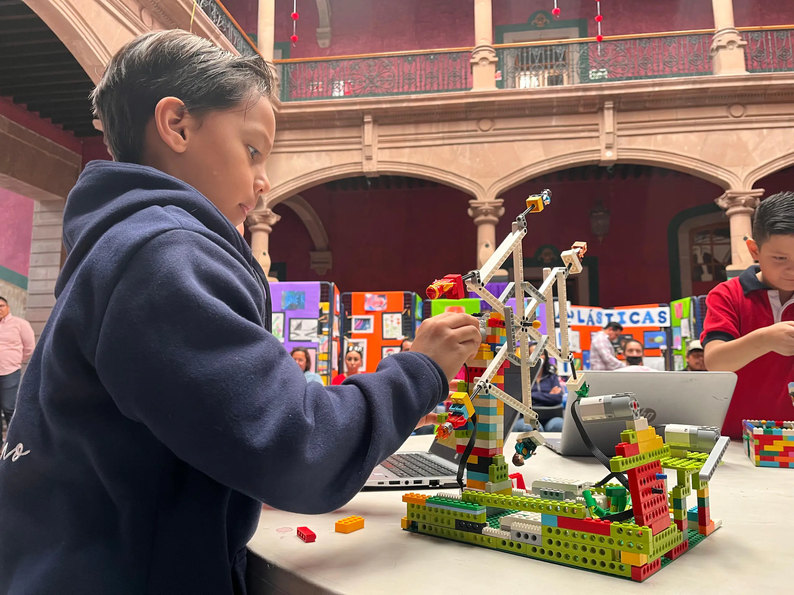 Alumno armando un robot LEGO en el patio colonial