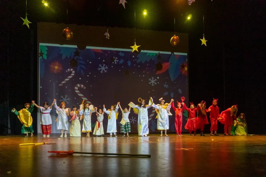 Niños de primaria en una presentación en escenario, con vestuario y luces