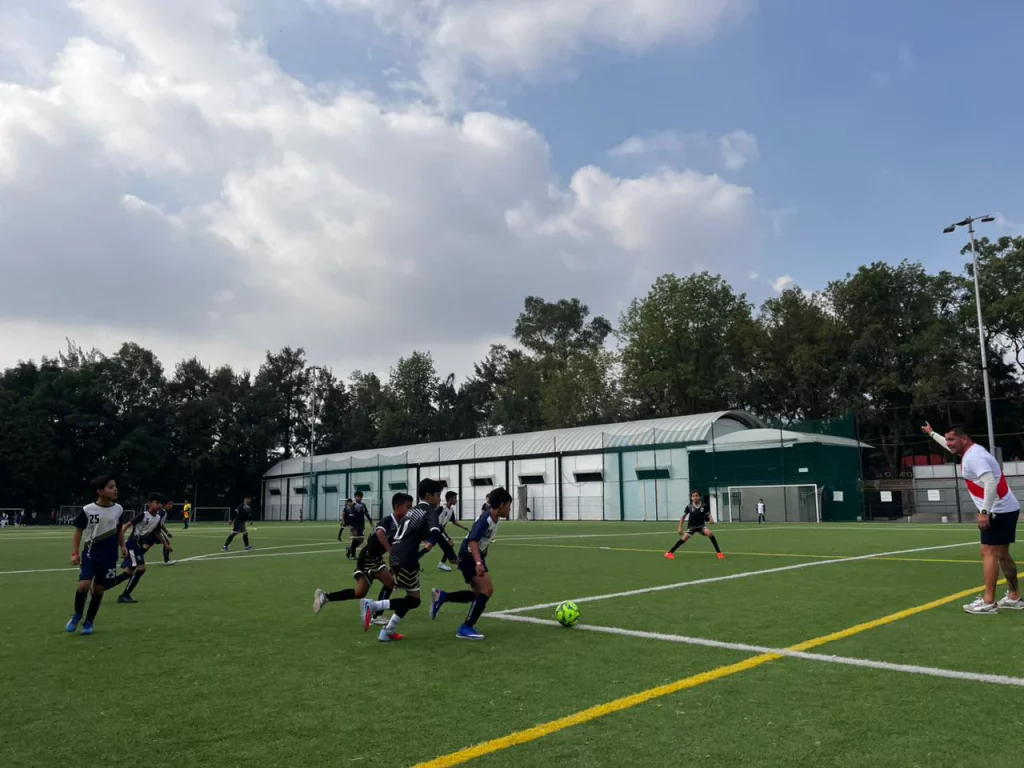 Alumnos jugando fútbol en el campo de pasto sintético